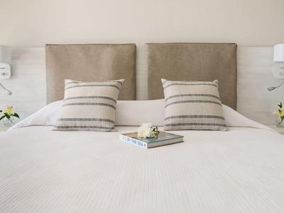 Gemütliches Doppelbett mit beigem Kopfteil, gestreiften Kissen und Buch auf weißer Bettdecke.