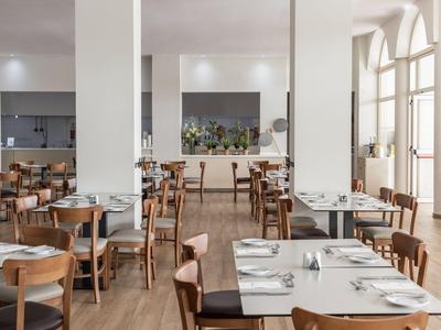 Jasna, nowoczesna restauracja z drewnianymi podłogami i dużymi oknami, stoły nakryte dla gości.