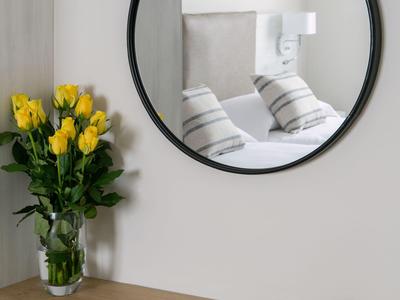 Specchio rotondo sopra scrivania in legno con occhiali da sole, libro e vaso con fiori gialli.