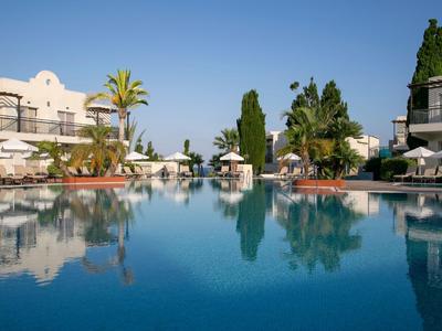 Grande piscina con acqua chiara e blu circondata da edifici bianchi e palme sotto il sole.