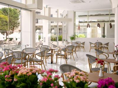 Helles Café mit Glaswänden, runden Holztischen und Stühlen, blühende Pflanzen als Dekoration.