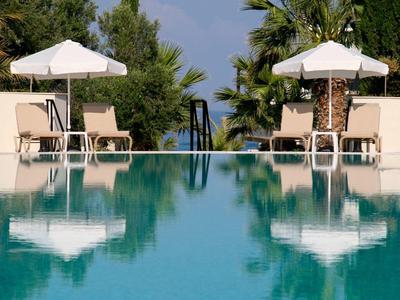 Schwimmbad mit blauer Wasserfläche, Liegestühlen und weißen Sonnenschirmen, Palmen im Hintergrund.