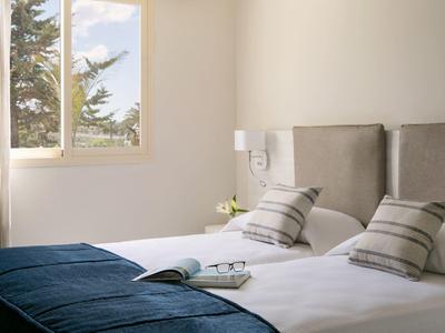 Helles Schlafzimmer mit großem Fenster, zwei Betten, grauen Kopfteilen und blauen Decken.