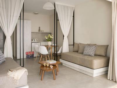 Helles Wohnzimmer mit weißen Vorhängen, brauner Couch, kleinem Holztisch und moderner Küchenzeile.