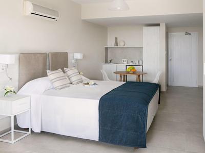 Helles Schlafzimmer mit Doppelbett, grauem Kopfteil, blauer Decke und minimalistischem weißen Mobiliar.