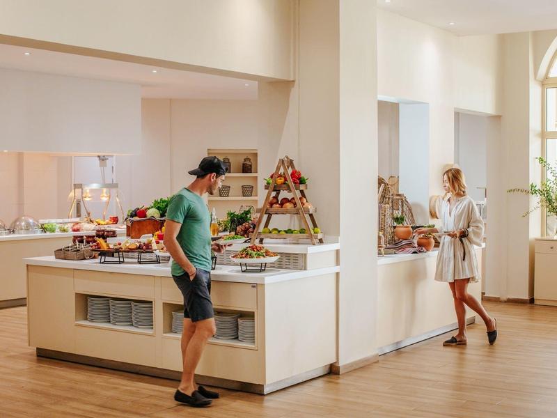 Ein heller Raum mit Buffet, zwei Personen wählen Speisen aus, moderne Ausstattung, Holzfußboden.