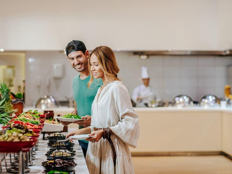 Ein Paar nimmt sich Essen an einem Buffet mit frischem Obst und Gemüse in einem hellen Raum.