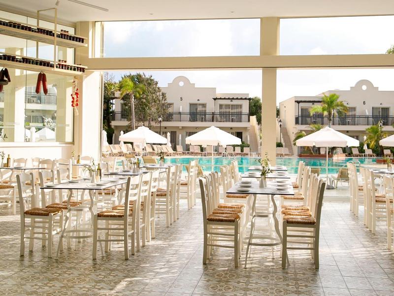 Heller, offener Speisesaal mit Holztischen und -stühlen, Blick auf Pool und Sonnenschirme draußen.