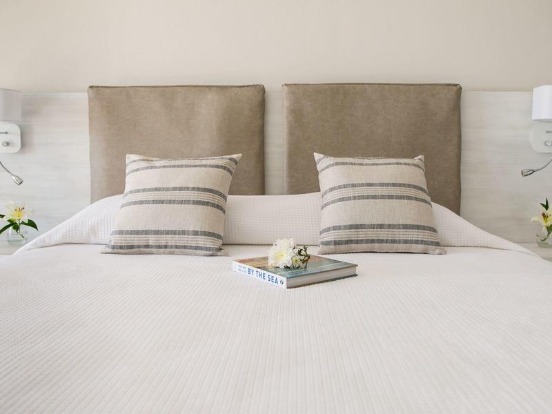 Gemütliches Doppelbett mit beigem Kopfteil, gestreiften Kissen und Buch auf weißer Bettdecke.