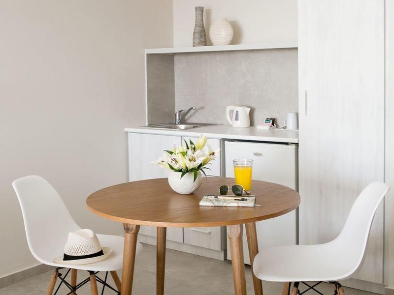 Moderner Essbereich mit runden Holztisch, zwei weißen Stühlen und kleiner Küchenzeile im Hintergrund.