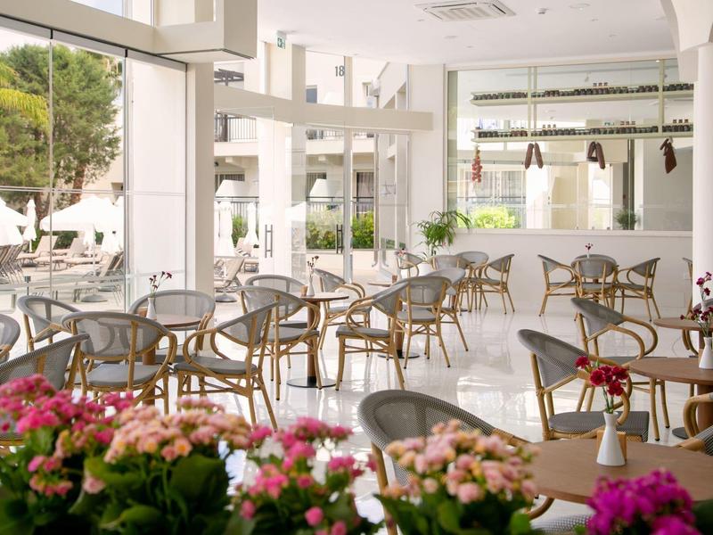 Helles Café mit Glaswänden, runden Holztischen und Stühlen, blühende Pflanzen als Dekoration.