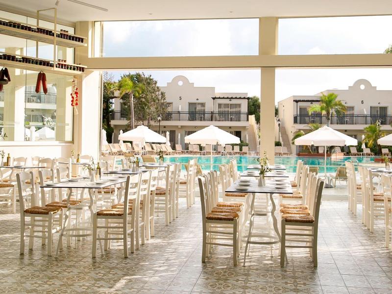 Heller Gastraum mit Holzstühlen und Tischen, Blick auf Pool und Sonnenschirme draußen.