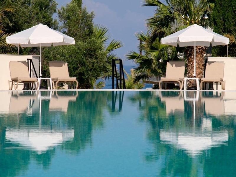 Schwimmbad mit blauer Wasserfläche, Liegestühlen und weißen Sonnenschirmen, Palmen im Hintergrund.