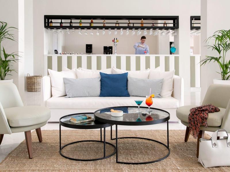 Modernes Wohnzimmer mit weißem Sofa, blauen Kissen, zwei runden Couchtischen und grünen Pflanzen.