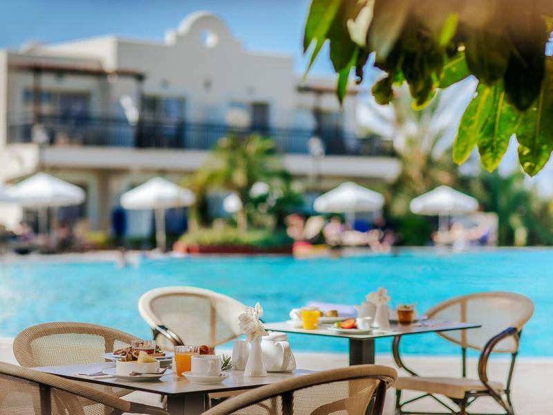 Außenbereich mit Tisch, Stühlen, Kaffeeservice und unscharfem Pool, Gebäuden im Hintergrund.