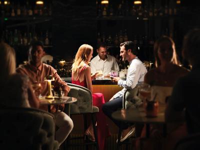 Menschen sitzen in einem dunklen Restaurant, sprechen und trinken an einem Tisch mit Kerzenlicht.