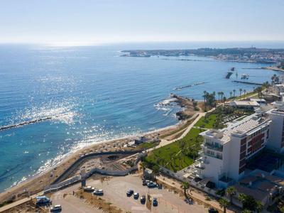Küstenstadt mit blauer See, Sandstrand, Promenade, Gebäuden und grünen Flächen bei klarem Himmel.