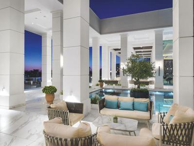 Moderner Outdoor-Wohnbereich mit weißen Säulen, Sitzmöbeln und Blick auf den Pool bei Abenddämmerung.