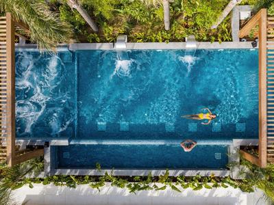 Widok z powietrza na basen z dwoma pływakami, otoczony zielenią.