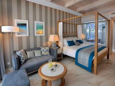 Gemütliches Schlafzimmer mit Himmelbett, Sofa, runder Holztisch und gestreifter Tapete.