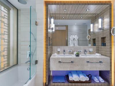 Modernes Badezimmer mit beiger Kachelwand, großem Spiegel und beleuchtetem Waschbecken.