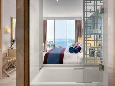 Moderner Badezimmerbereich mit Badewanne, Sicht auf Schlafzimmer und Meer durch großes Fenster.