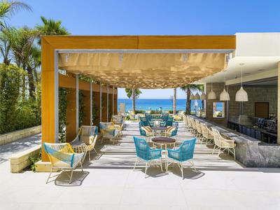 Moderner Außenbereich mit blauen Stühlen, Holzdach und Blick aufs Meer bei klarem Himmel.