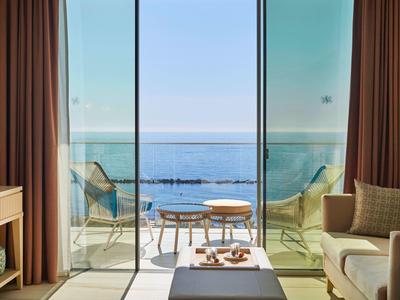 Moderner Wohnraum mit beige Sofa, Glasfront und Blick auf Terrasse und blaues Meer.