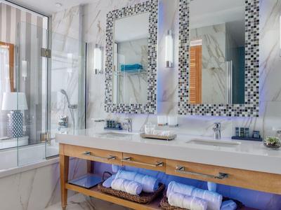 Helles Badezimmer mit Doppelwaschbecken, Mosaikspiegeln und Holzregal unter Marmorarbeitsplatte.