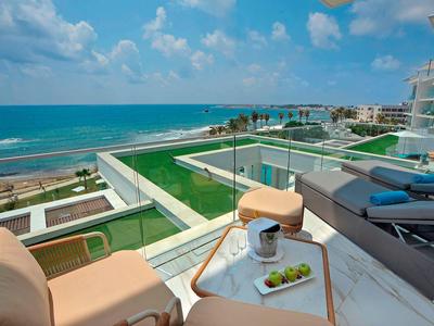 Balkon mit Lounge-Möbeln, Blick auf grünes Dach und blauen Ozean unter bewölktem Himmel.
