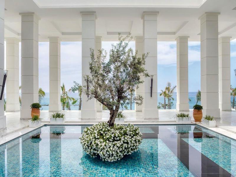 Großer heller Pool in modernem Gebäude mit weißen Säulen und Pflanzen in der Mitte.