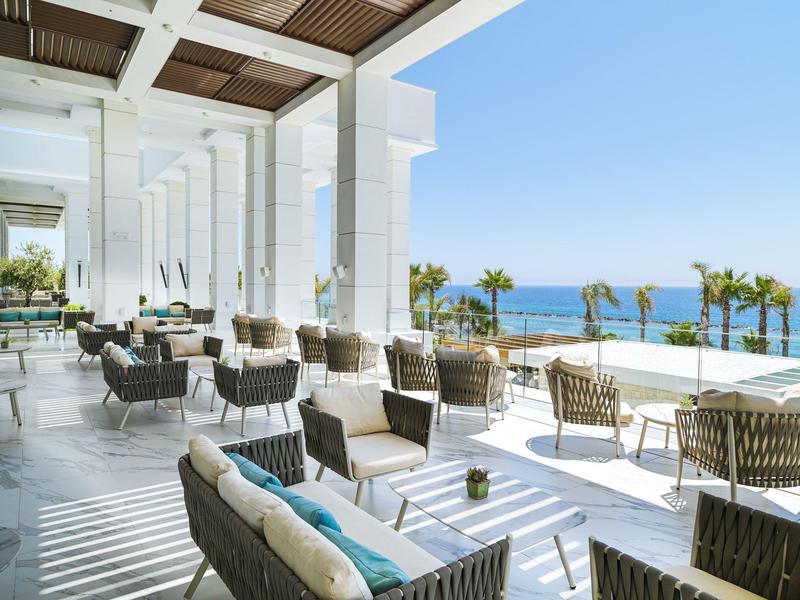 Terrassenlounge mit modernen Sesseln, Glasgeländer und Meerblick unter klarem Himmel.