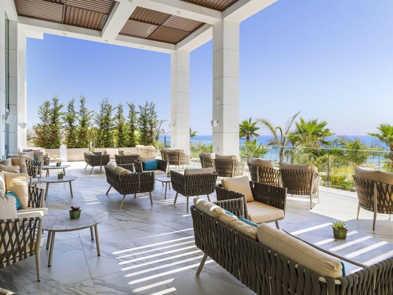 Offene Terrasse mit modernen Korbsesseln und Blick auf Meer und blauen Himmel unter hellem Sonnenschein.