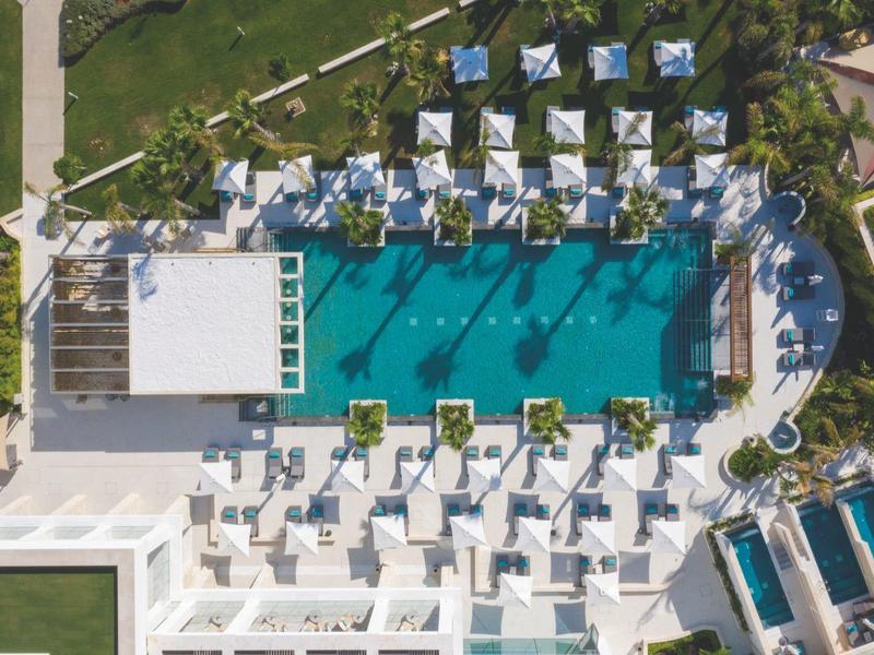 Luftaufnahme eines rechteckigen Pools mit weißen Liegen und Sonnenschirmen in grünem Garten.