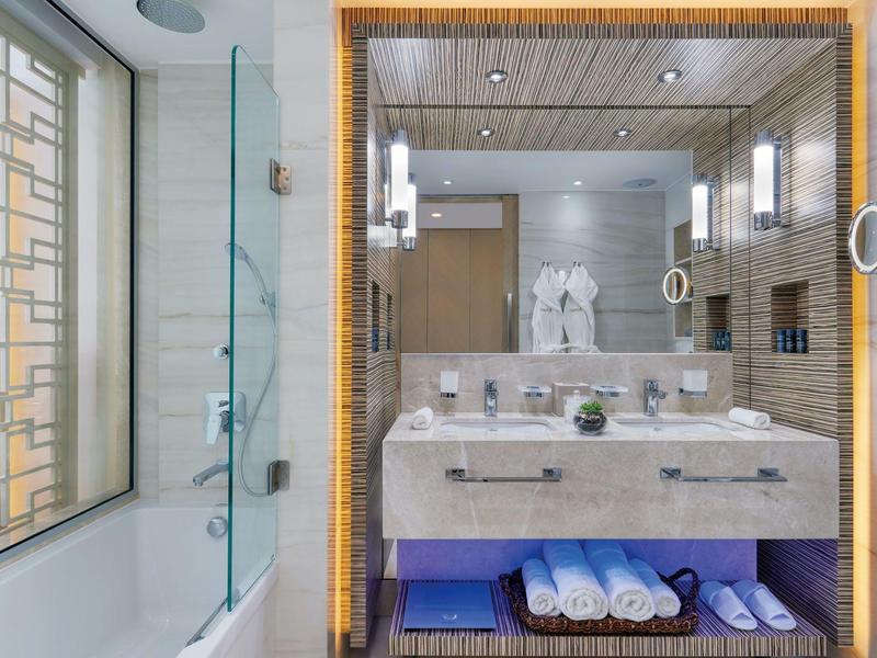 Modernes Badezimmer mit beiger Kachelwand, großem Spiegel und beleuchtetem Waschbecken.