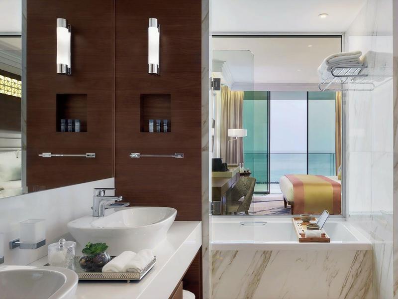 Moderne Bad mit zwei weißen Waschbecken, brauner Holzwand, großer Spiegel und Glaswand zum Wohnzimmer.