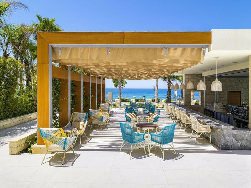 Moderner Außenbereich mit blauen Stühlen, Holzdach und Blick aufs Meer bei klarem Himmel.