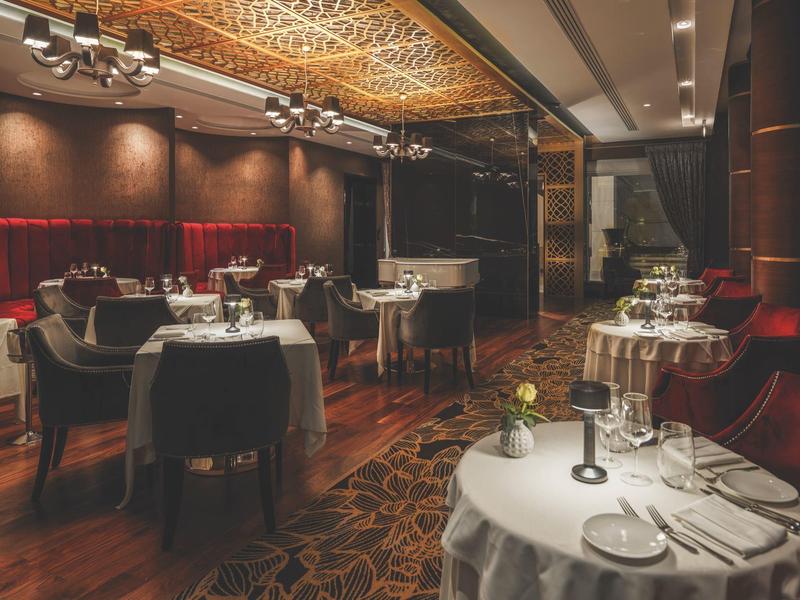 Elegantes Restaurant mit gedeckten Tischen, dunklem Holz und warmem Deckenmuster.