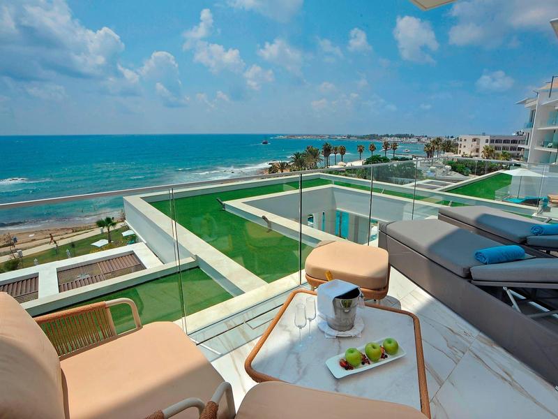 Balkon mit Lounge-Möbeln, Blick auf grünes Dach und blauen Ozean unter bewölktem Himmel.