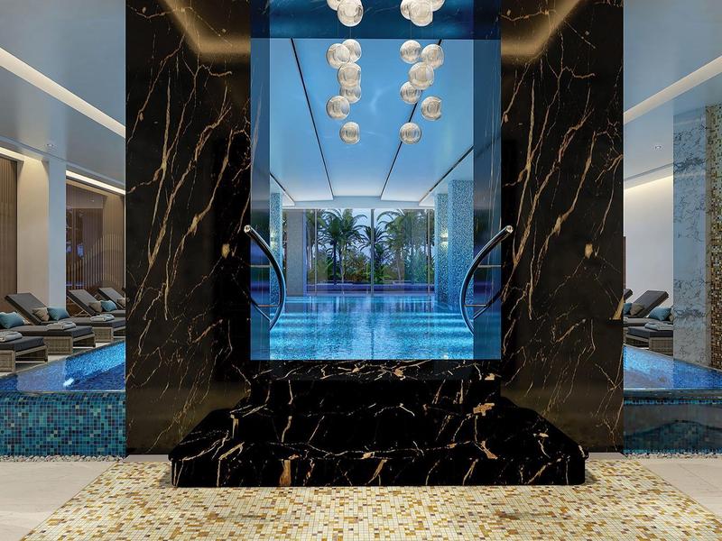 Moderner Indoor-Pool mit schwarzem Marmortresen, Glaswand und glühender Deckenbeleuchtung.