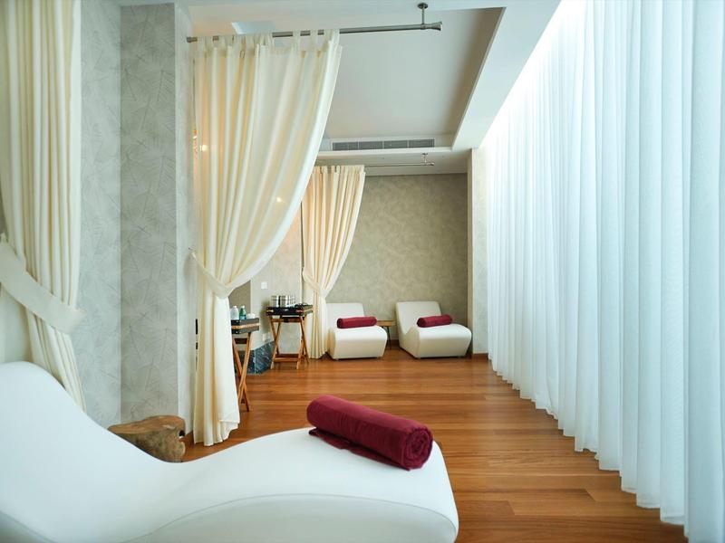 Moderner Wellnessraum mit weißen Liegen, Holzfußboden und lichtdurchlässigen Vorhängen.