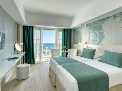 Chambre d'hôtel moderne avec lit double et vue sur la mer depuis le balcon.