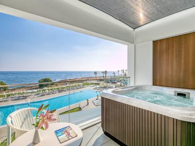 Balkon mit Whirlpool, weißen Stühlen, Tisch und Meerblick bei klarem Himmel am Tag.