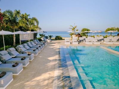 Piscine d'hôtel avec chaises longues et vue sur la mer sous un ciel bleu