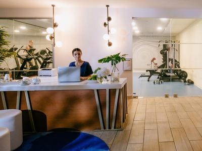 Hall d'hôtel moderne avec réception et employé utilisant un ordinateur portable derrière un comptoir en bois.