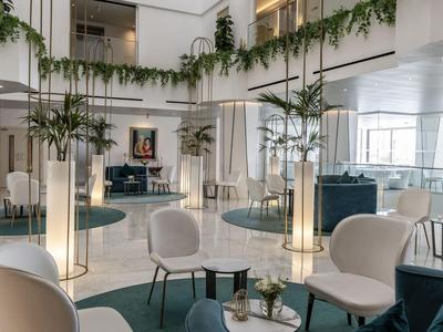 Lobby di hotel moderna con poltrone bianche, tavoli rotondi e piante verdi in un ambiente elegante.
