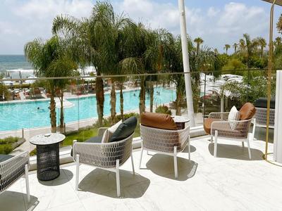 Terrasse moderne avec chaises donnant sur la piscine et les palmiers de l'hôtel.