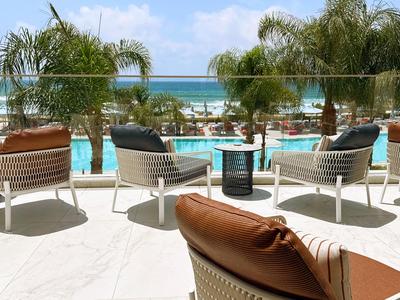 Vue sur la piscine et la mer depuis une terrasse avec des chaises et des palmiers.