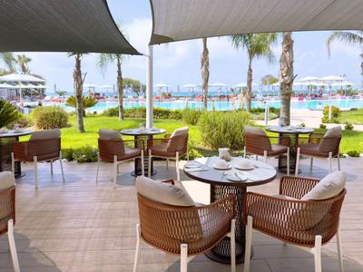 Espace de restauration avec chaises en osier et tables sous des auvents, vue sur des palmiers et une piscine.