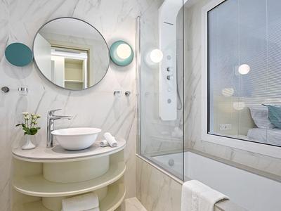 Helles Badezimmer mit rundem Spiegel, Waschbecken auf Ablage und Badewanne neben großem Fenster.